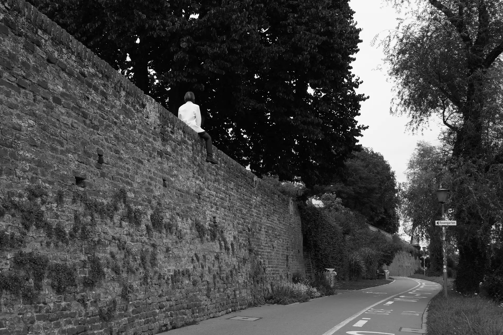 A person with a white top sitting on a old wall above 4 meter above ground.