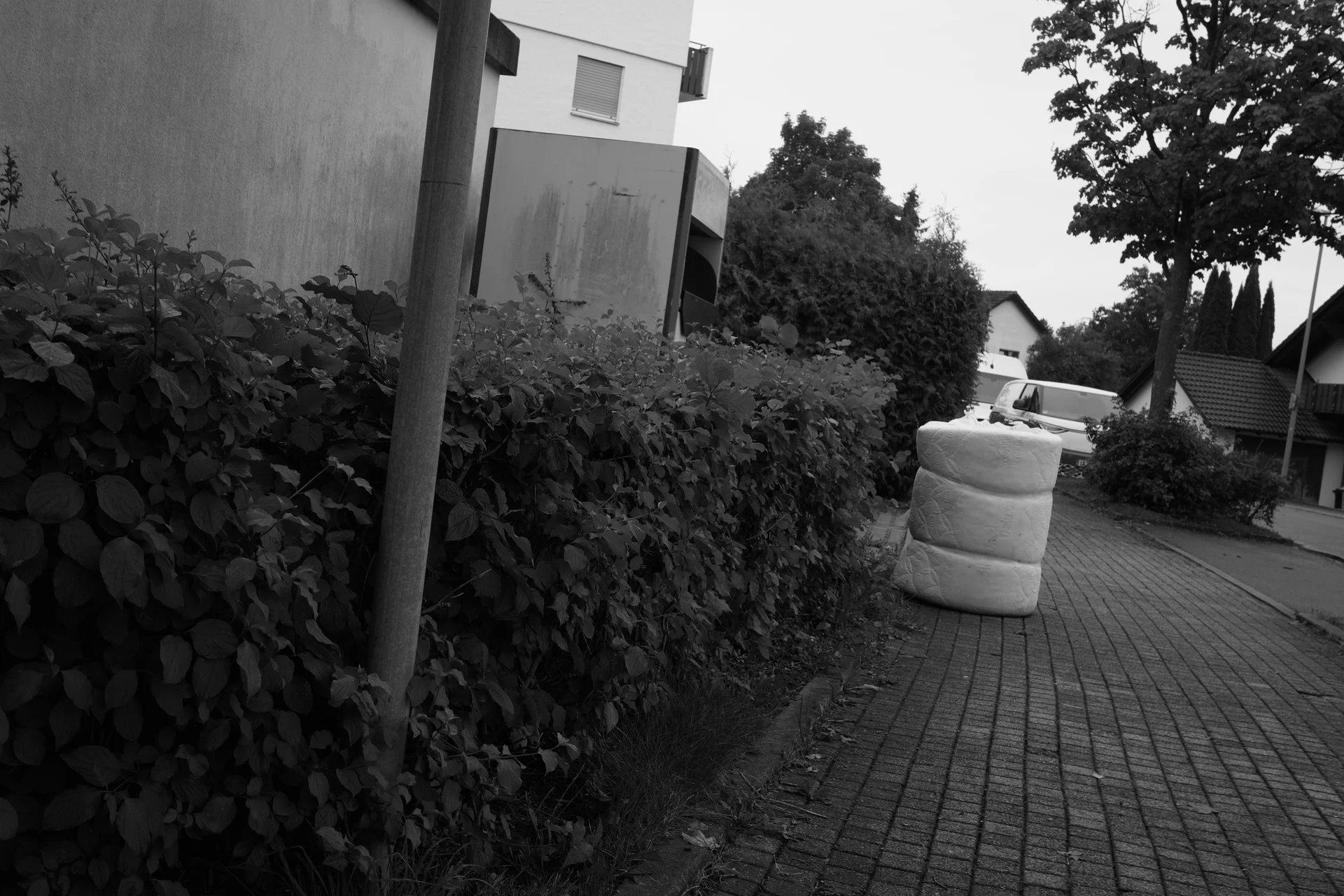 A strapped but used looking mattress standing on a sidewalk.