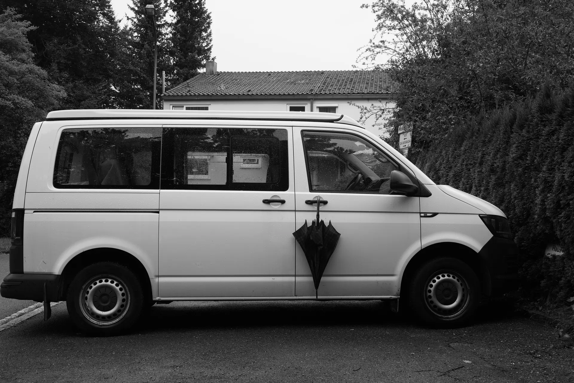A umbrella hanged at the door handle of a van standing at a parking.