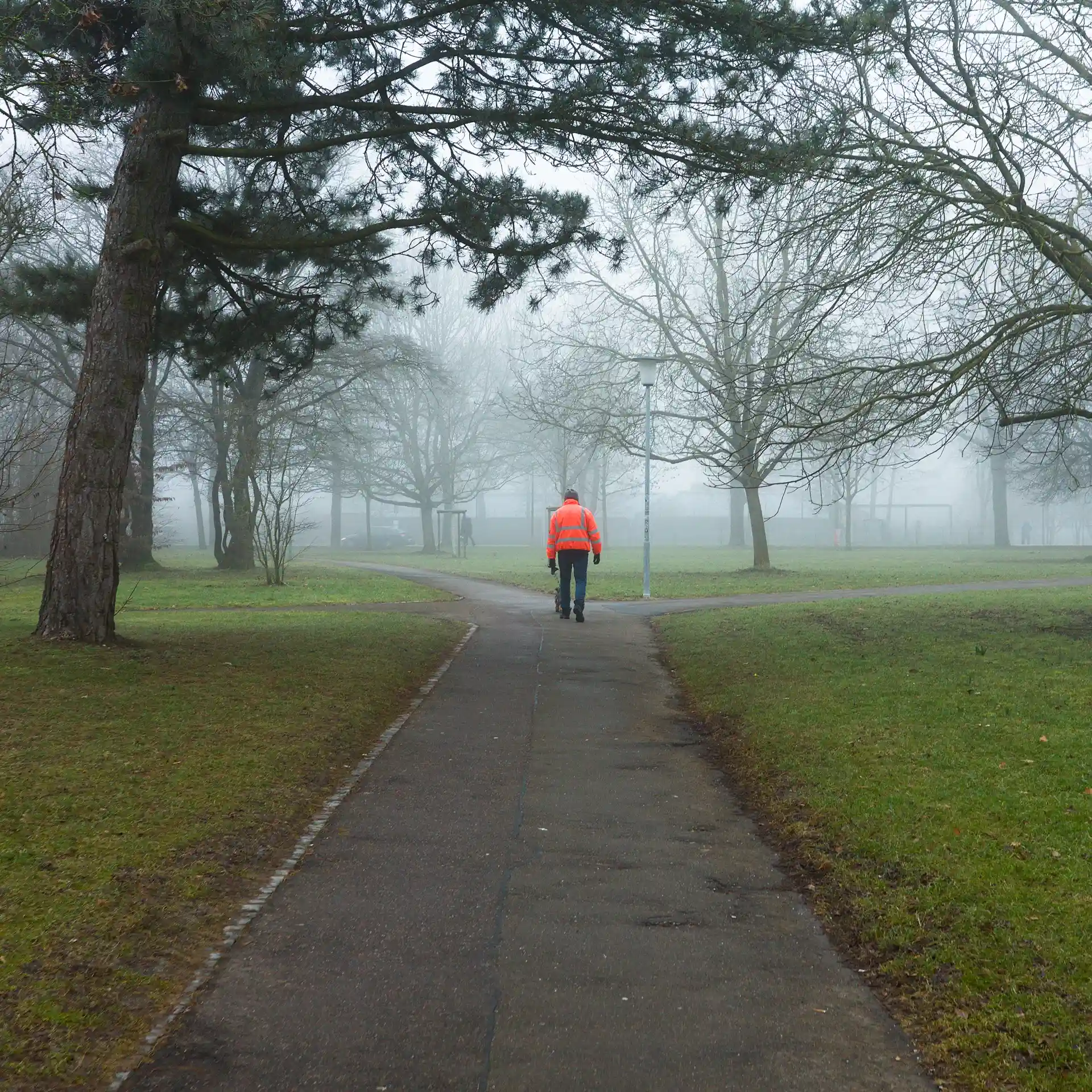 A person with a bright orange jacket on a pedestrian way in a park.